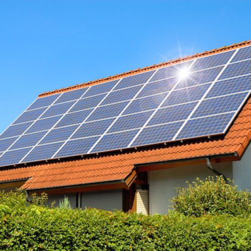 Solar panel on a red roof reflecting the sun and the cloudless blue sky